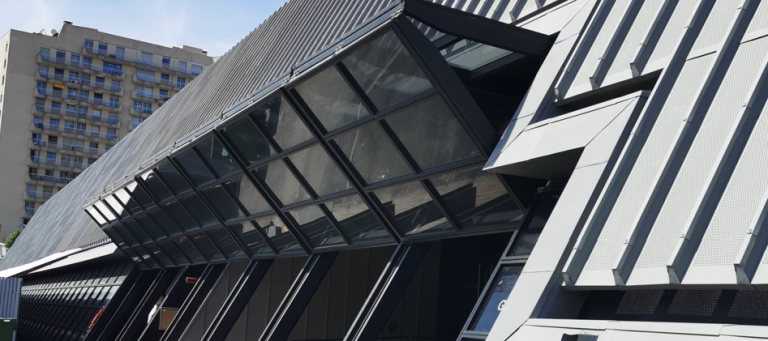Angular dark metal facade of a public building, with slanted glazing and perforated aluminium cladding