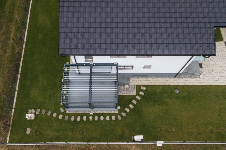 Overhead view of a bioclimatic pergola with open louvres beside a house with a dark tiled roof