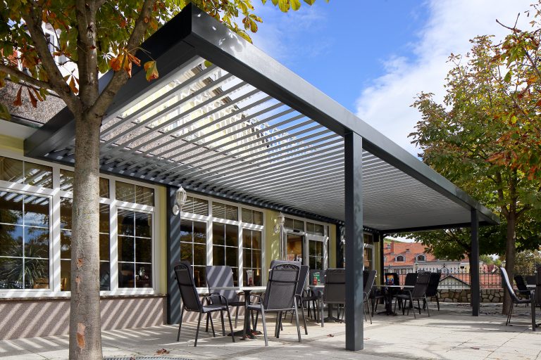 Anthracite bioclimatic pergola with open louvres over a restaurant terrace, with tables and chairs beneath