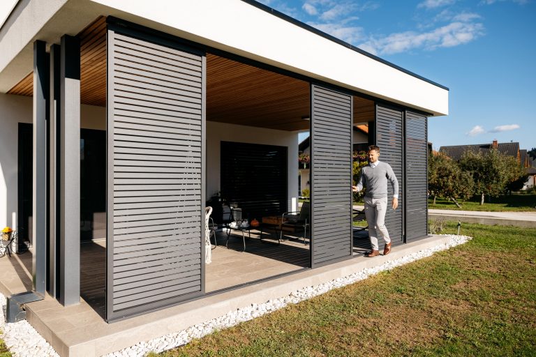 Grey sliding shutters along the covered terrace of a modern house, one panel slid open