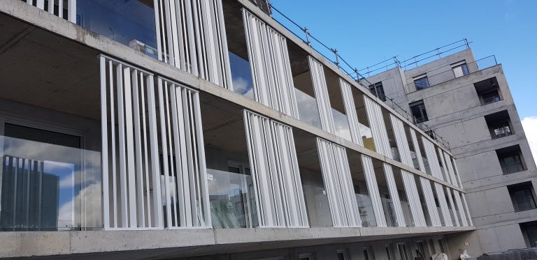White vertical aluminium sunbreakers along the concrete balconies of an apartment building under construction