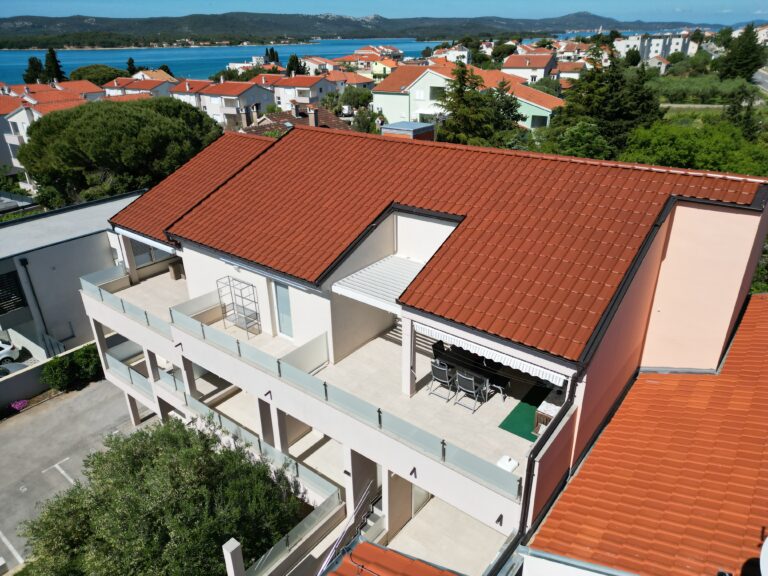 Aerial view of a coastal apartment building with a terracotta tiled roof and a Soltec awning shading the top-floor terrace, with the sea beyond