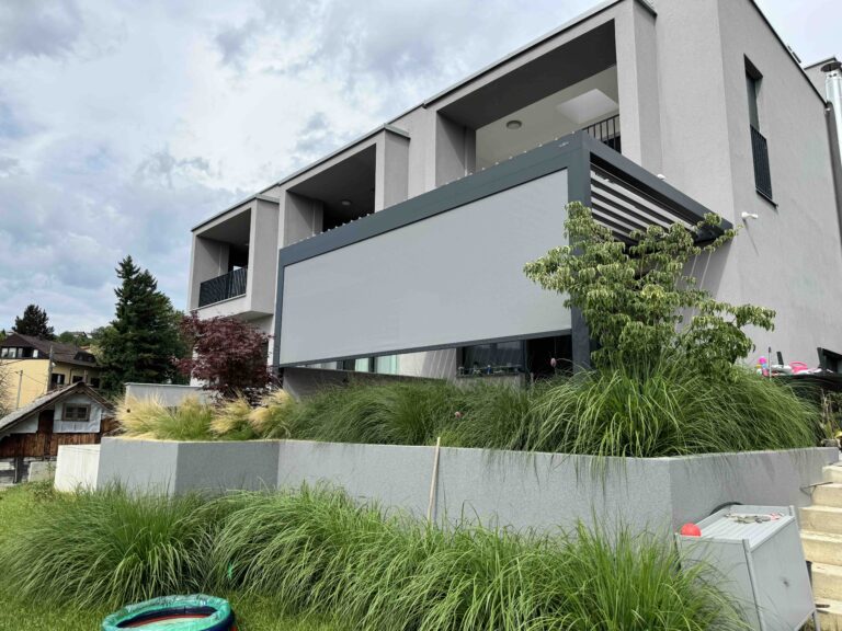 Bioclimatic pergola on the terrace of a modern grey house, with a light screen blind lowered along one side
