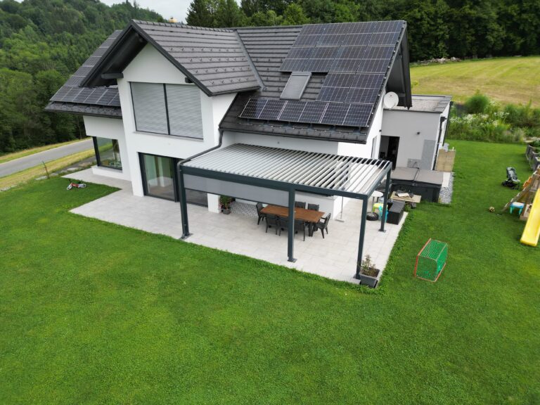 Aerial view of a family house with roof solar panels and an anthracite bioclimatic pergola with open louvres over the terrace